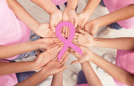 10 hands meeting in the middle of a circle with a pink ribbon in the middle